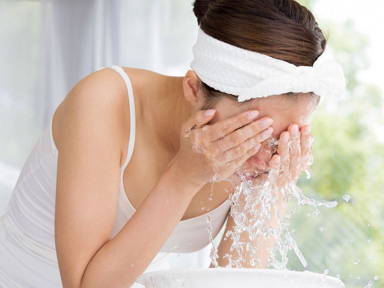 Frau wäscht sich mit Wasser das Gesicht