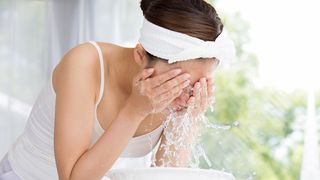 Frau wäscht sich mit Wasser das Gesicht