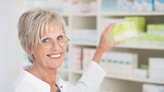 Ältere Apothekerin holt Medikamente aus dem Regal