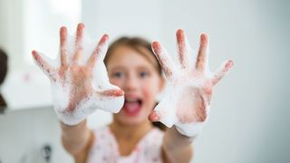 Kind zeigt begeistert seine eingeseiften Hände in die kamera