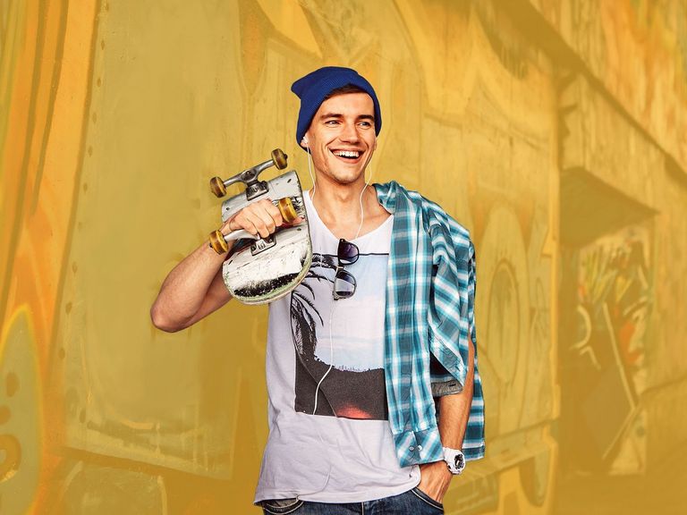 Junger Skater steht mit Skateboard an einer Hauswand	