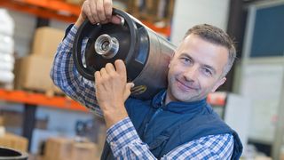 Schweres Heben und Tragen im Beruf In einem Lager arbeitender Mann trägt etwas schweres auf der Schulter