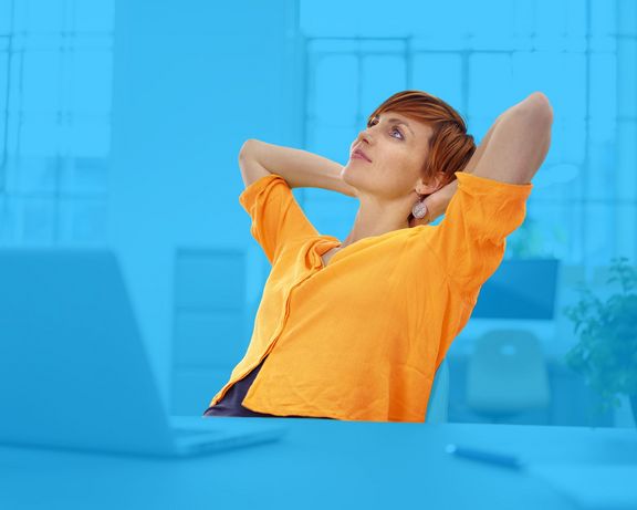 Frau am Schreibtisch mit Händen hinter dem Kopf