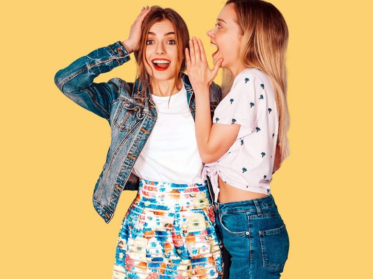 Junge Frau flüstert einer anderen jungen Frau leise etwas ins Ohr