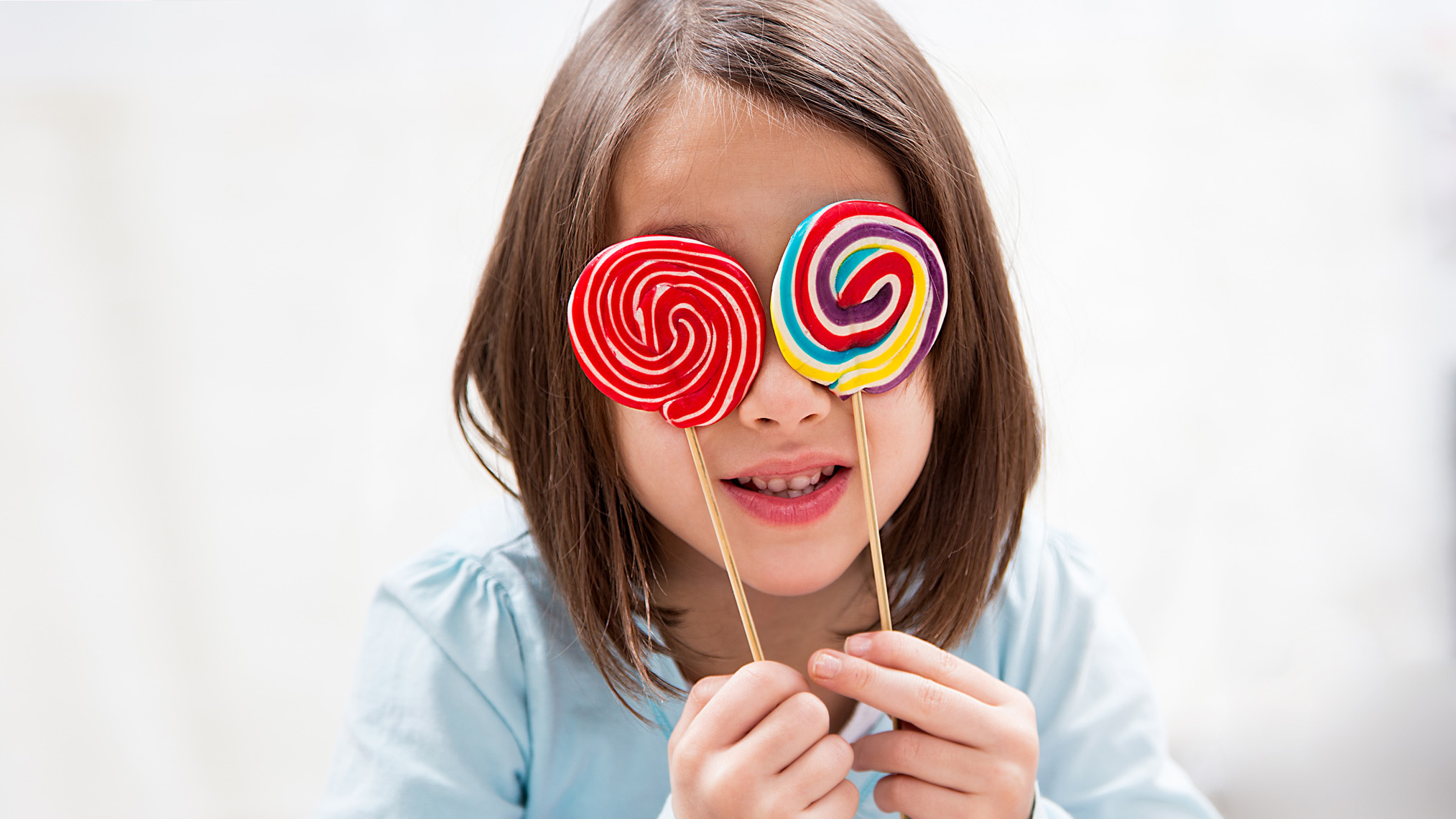 Kleines Mädchen hält sich zwei bunte Lutscher vor die Augen