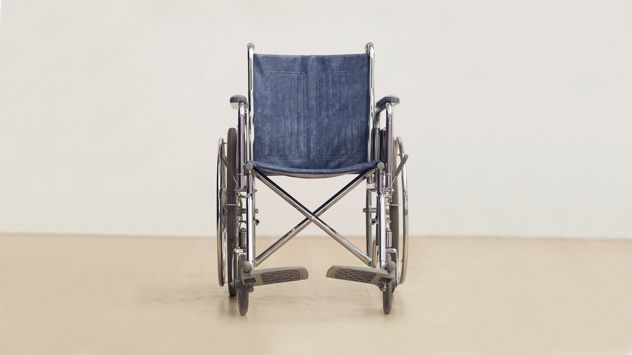 ein leerer Rollstuhl vor eine weißen Wand