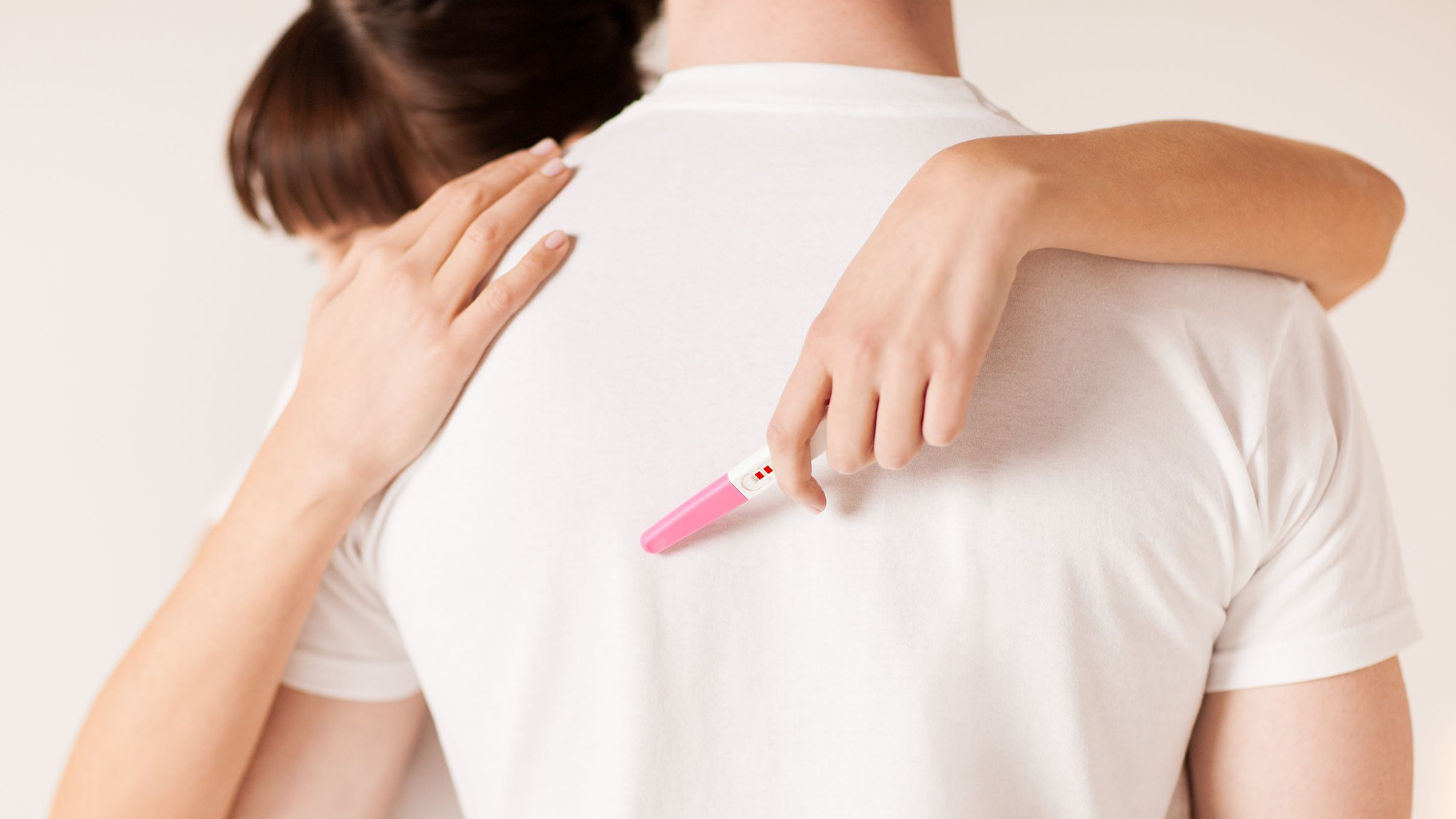 Frau mit einem Schwangerschaftstest in der Hand im Arm eines Mannes