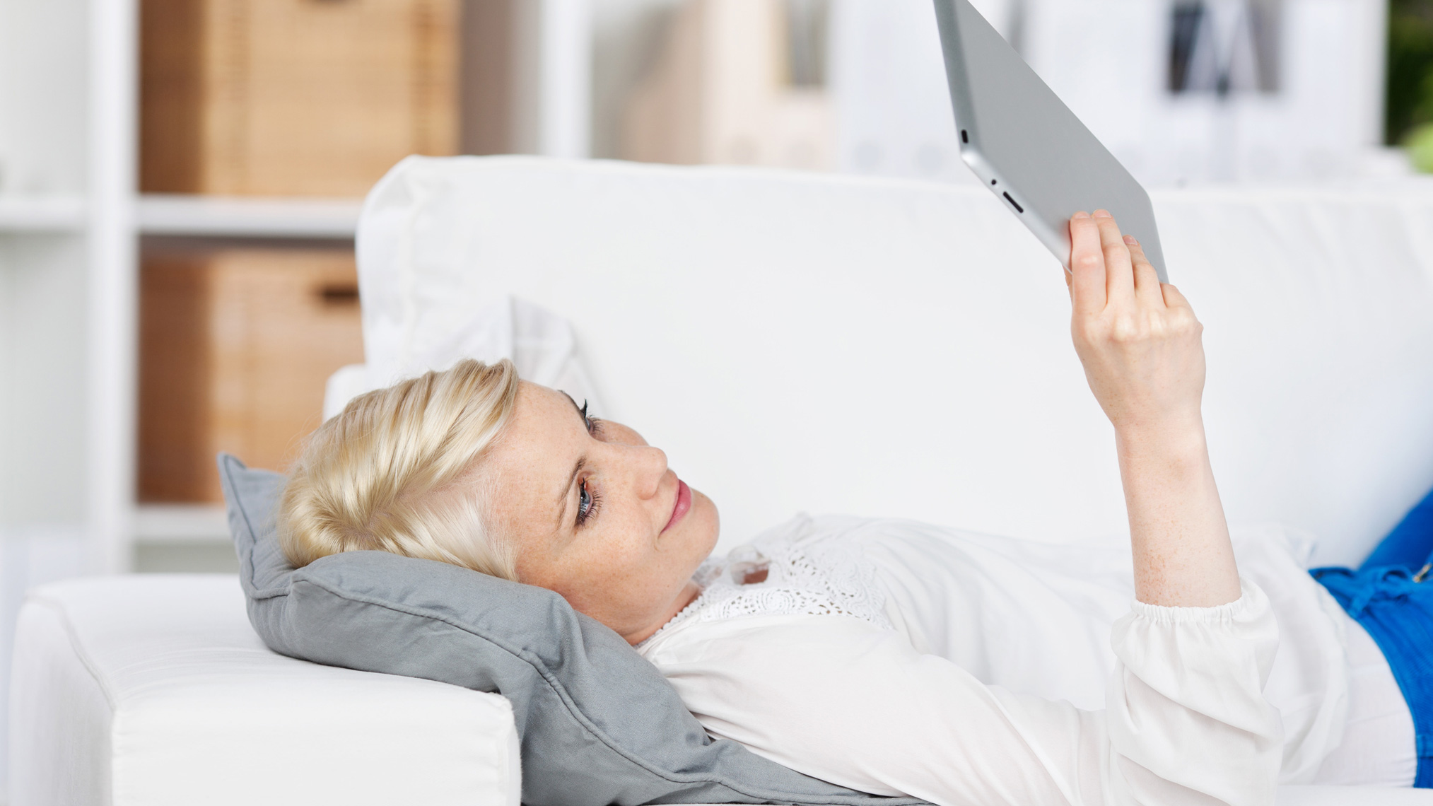 Frau liegt auf Sofa und liest auf Tablet