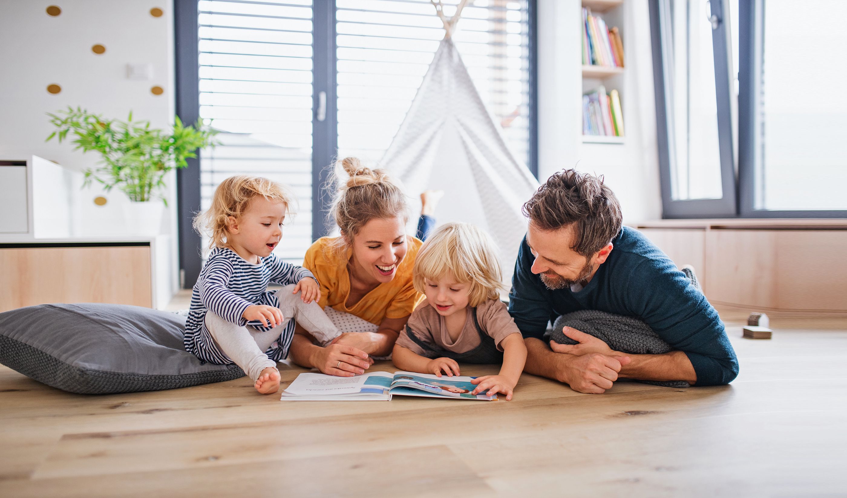 Familie mit 2 Kindern lesen im Kinderzimmer auf dem Fußboden gemeinsam mit viel Freude ein Buch