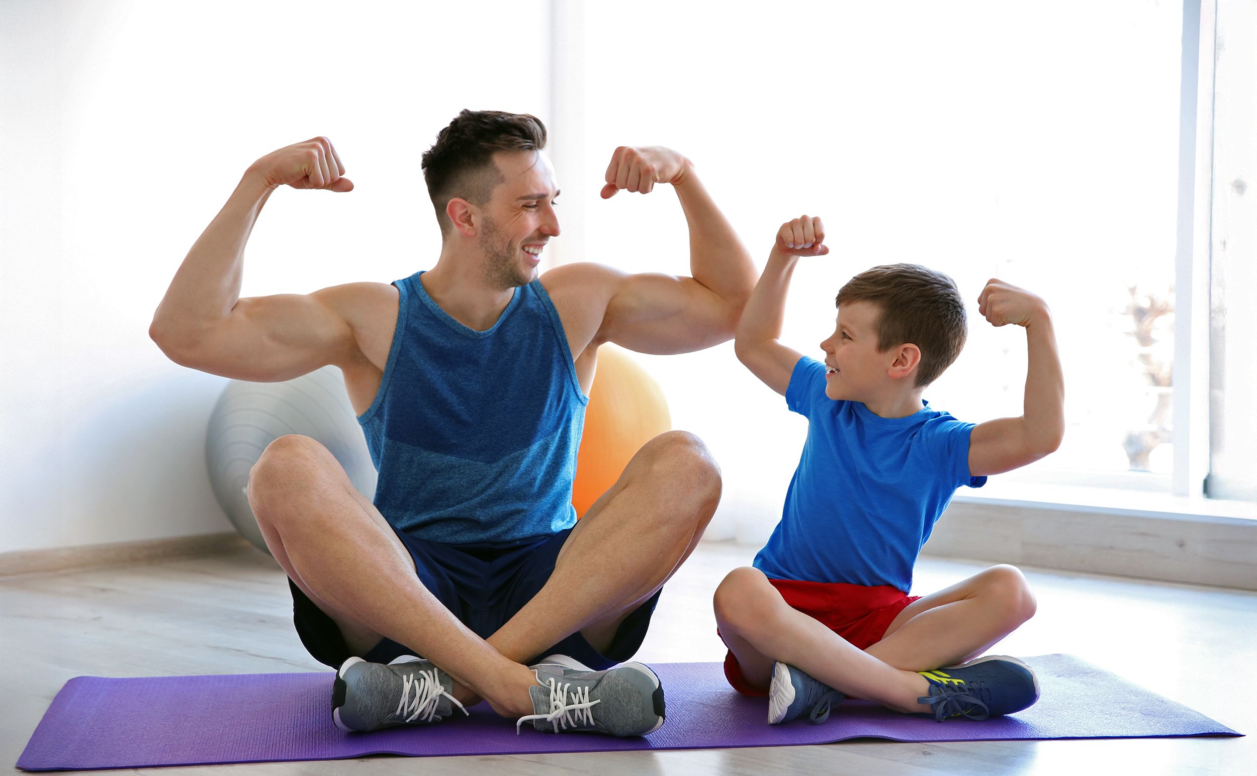 Vater und Sohn zeigen im Schneidersitz sitzend ihr Armmuskeln