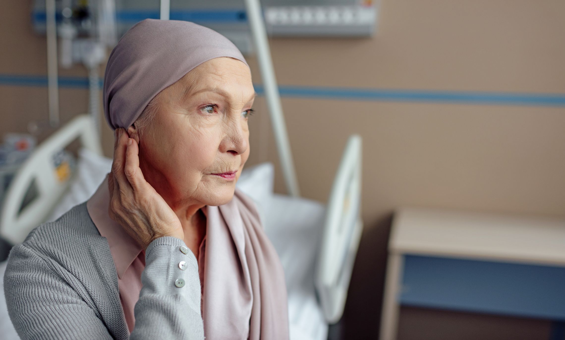 Krebskranke ältere Frau sitzt gedankenverloren in einem Krankenhauszimmer
