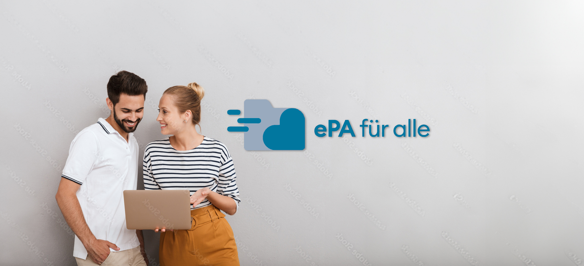 Mann und Frau stehen vor einer grauen Wand und schauen auf den Bildschirm eines Laptops	