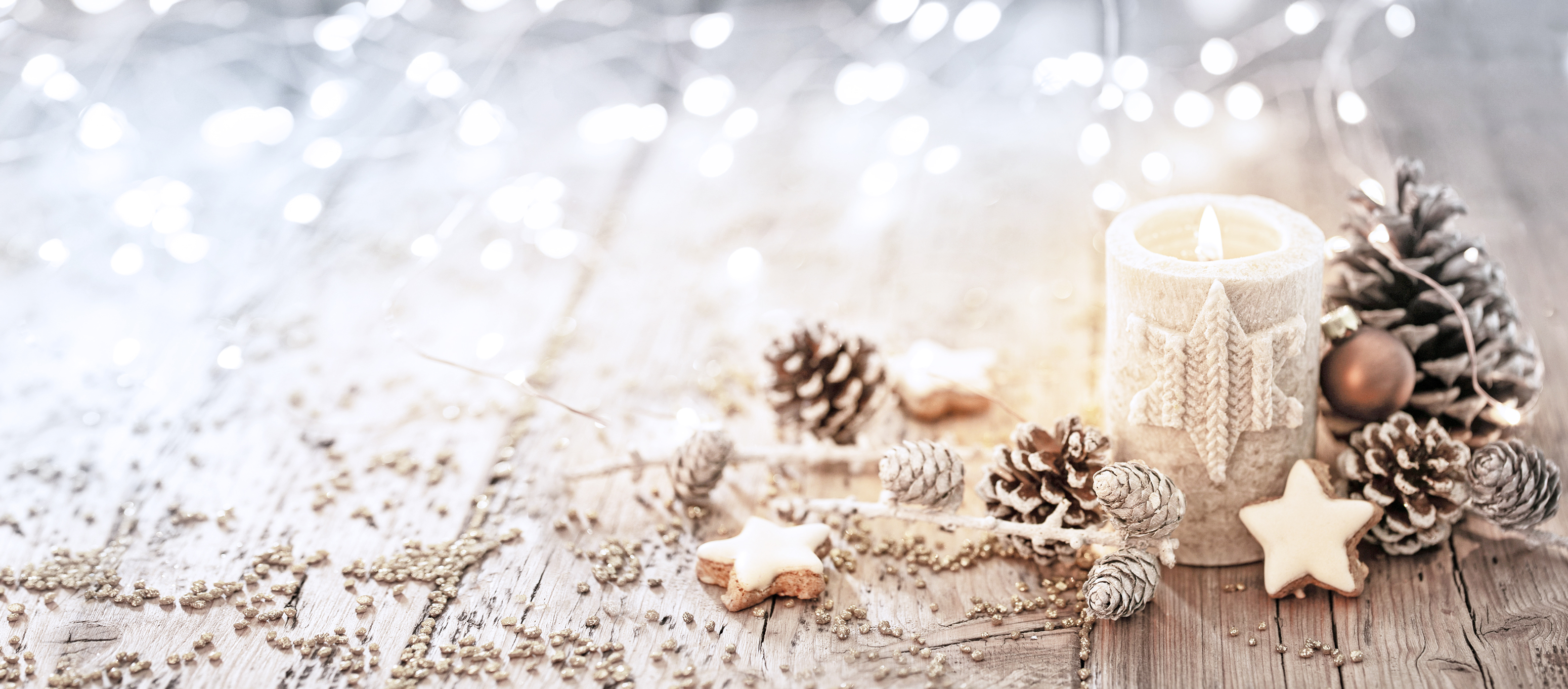 Kerze, Tannenzapfen und Zimtsterne liegen weihnachtlich-dekorativ auf einem Holztisch
