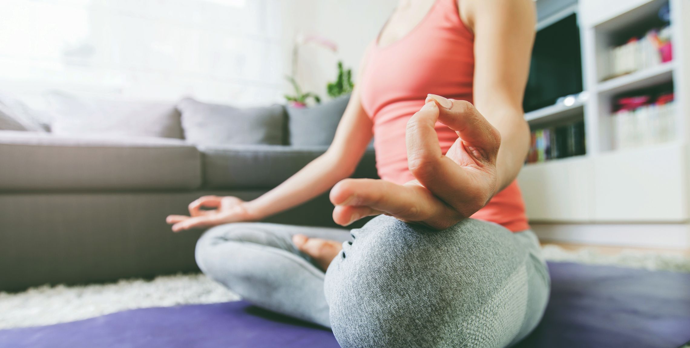 Frau sitzt entspannt im Yoga-Sitz auf einer Matte im Wohnzimmer
