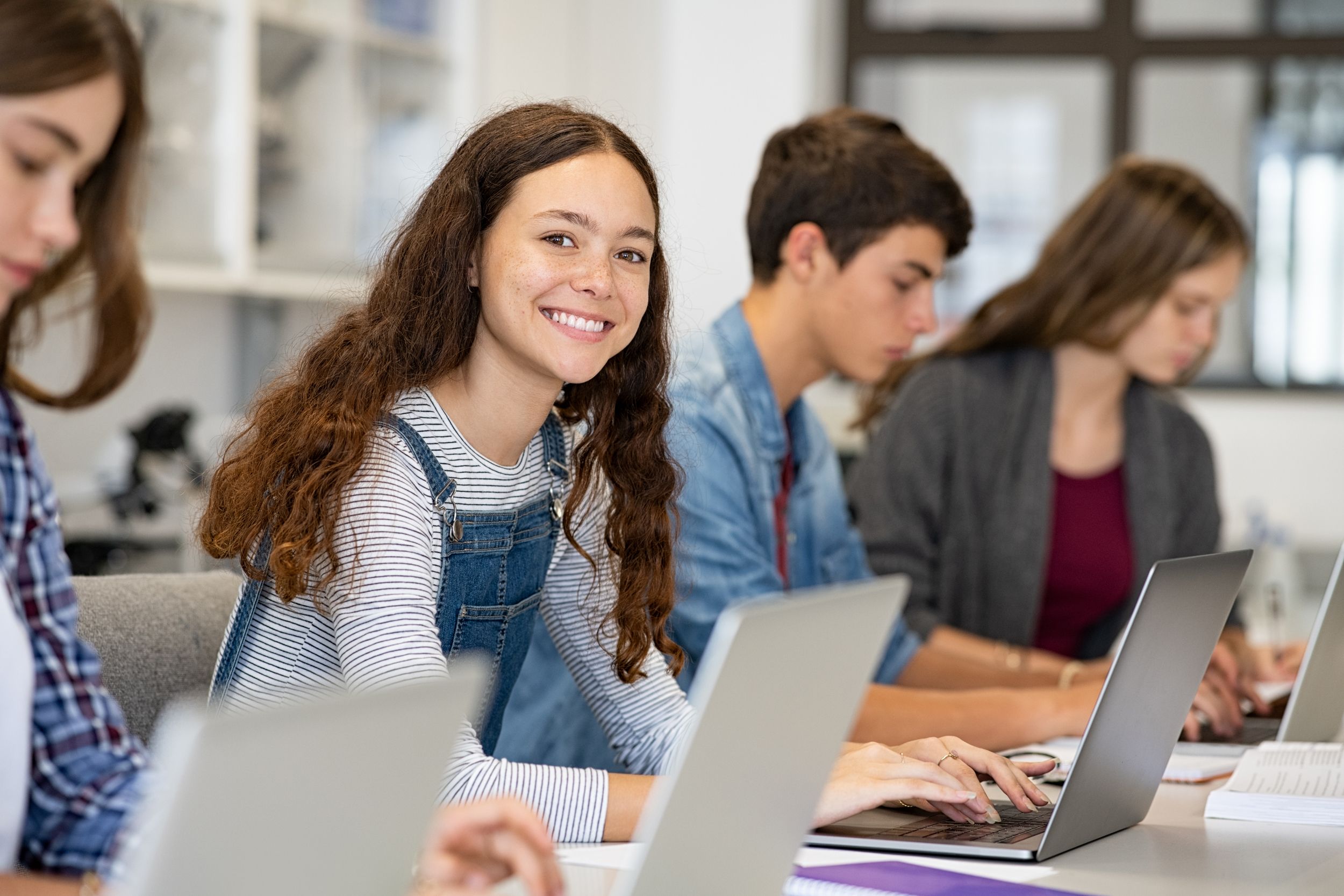 Schüler sitzen in der Schule am Laptop und ein Mädchen lächelt in die Kamera