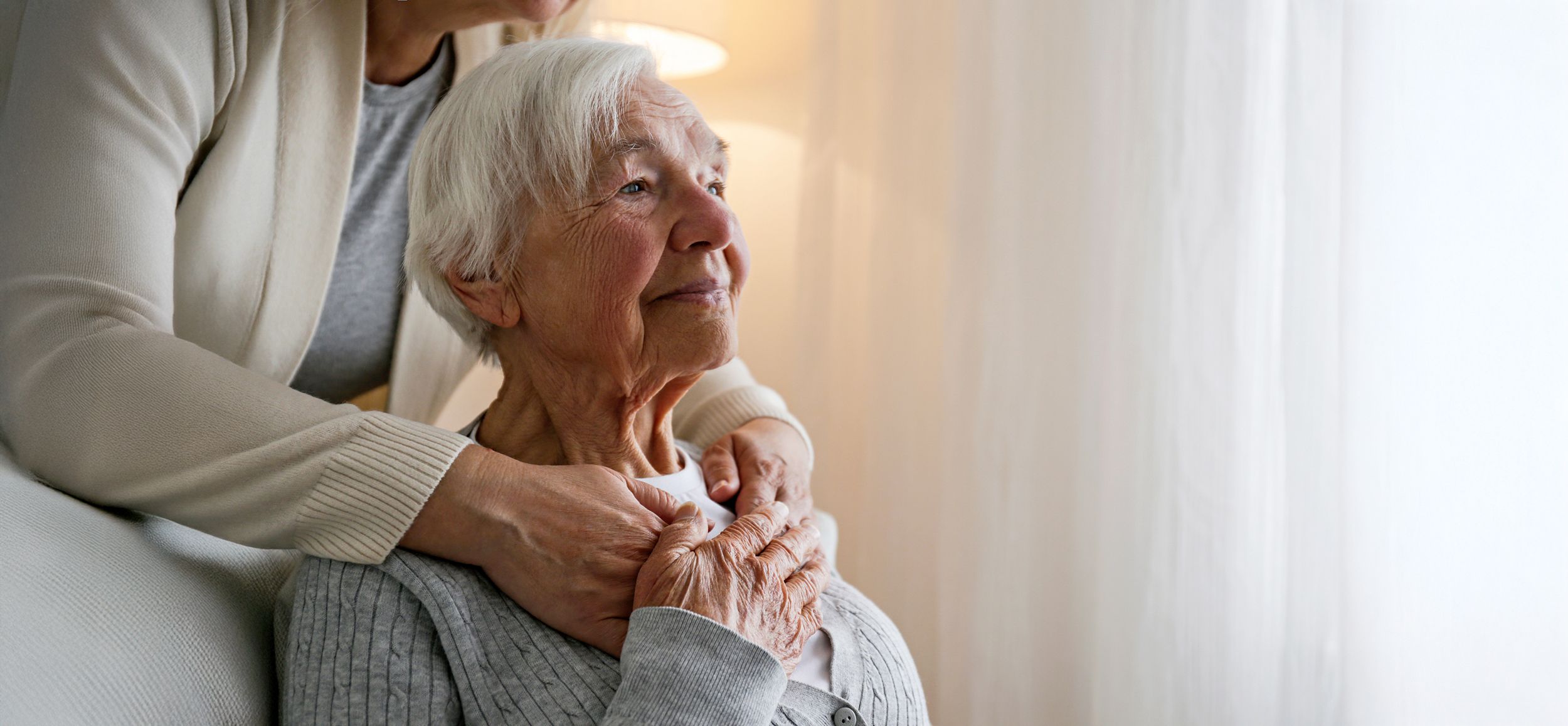 Frau betreut eine Pflegebedürftige und legt ihre Arme um deren Schultern