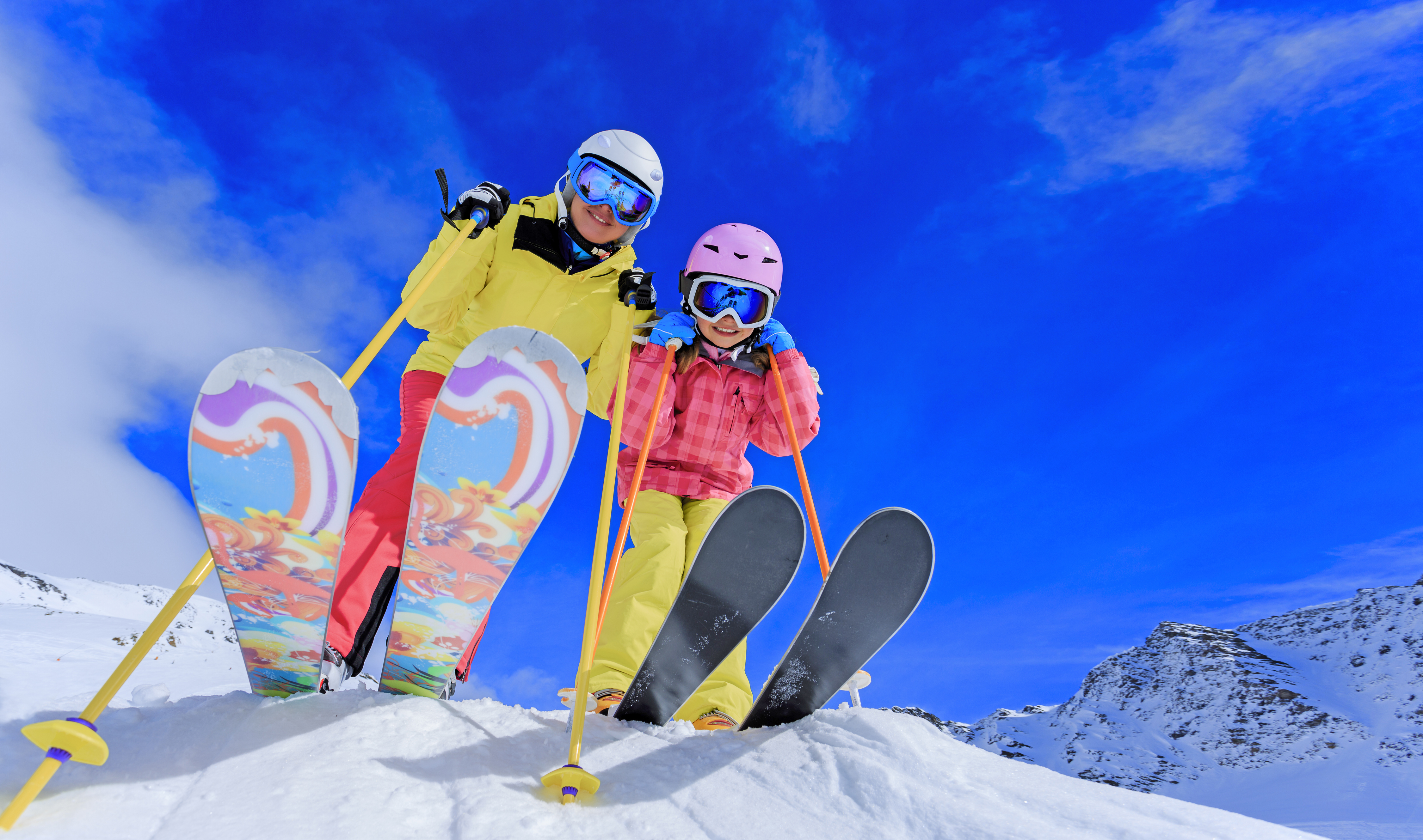 Mutter und Tochter in kompletter farbenfroher Skiausrüstung stehen lachend im Schnee