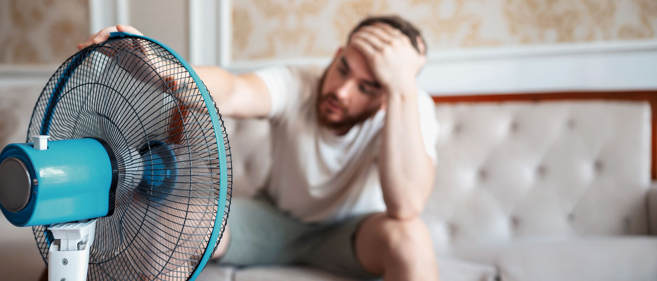 Mann im Wohnzimmer vor einem Ventilator sitzend