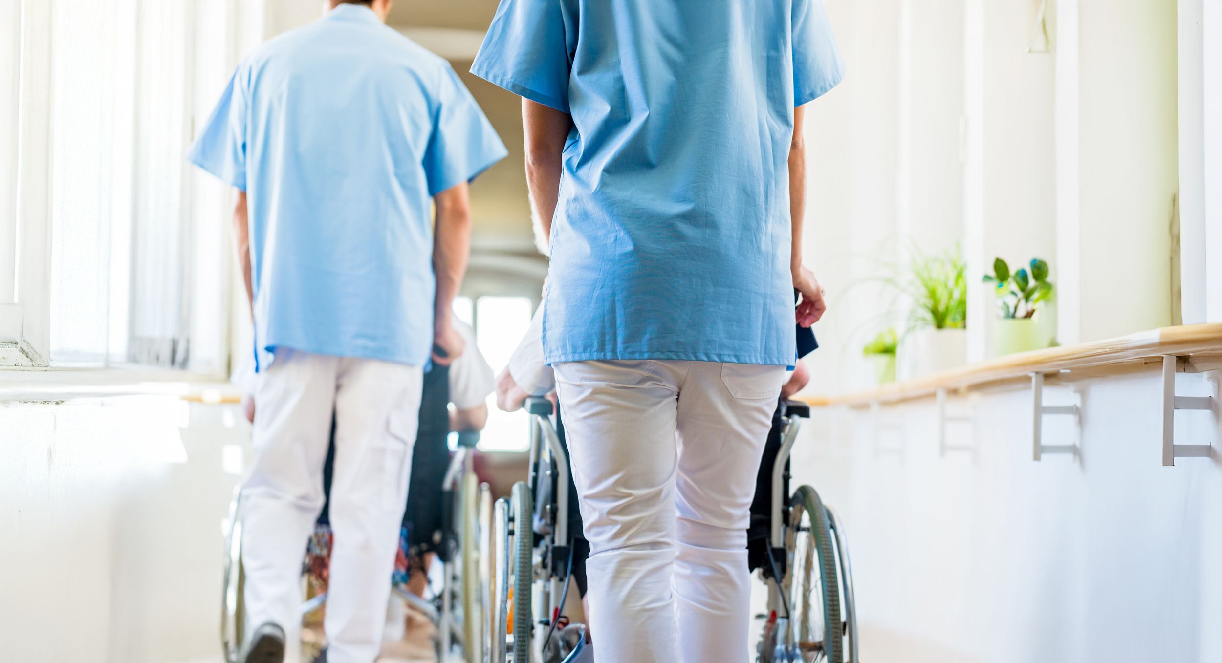 Zwei Stationspfleger schieben Rollstühle mit Pflegebedürftigen