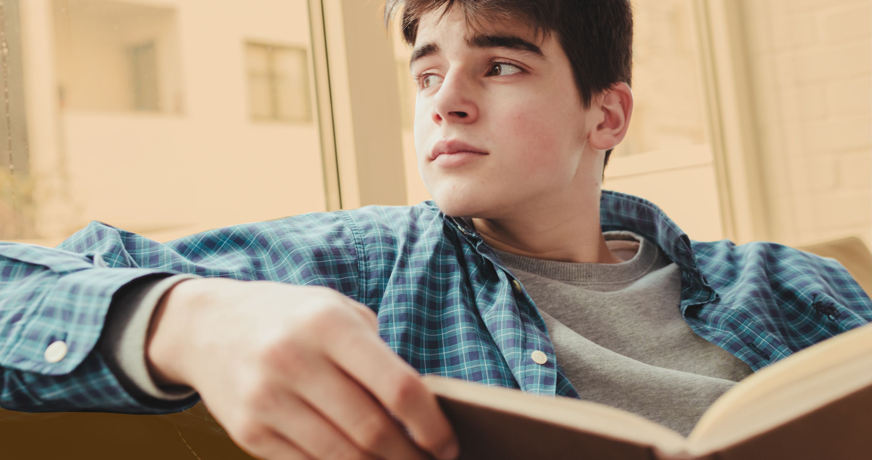 Jugendlicher sitzt verträumt auf einer Couch und hält ein Buch in den Händen