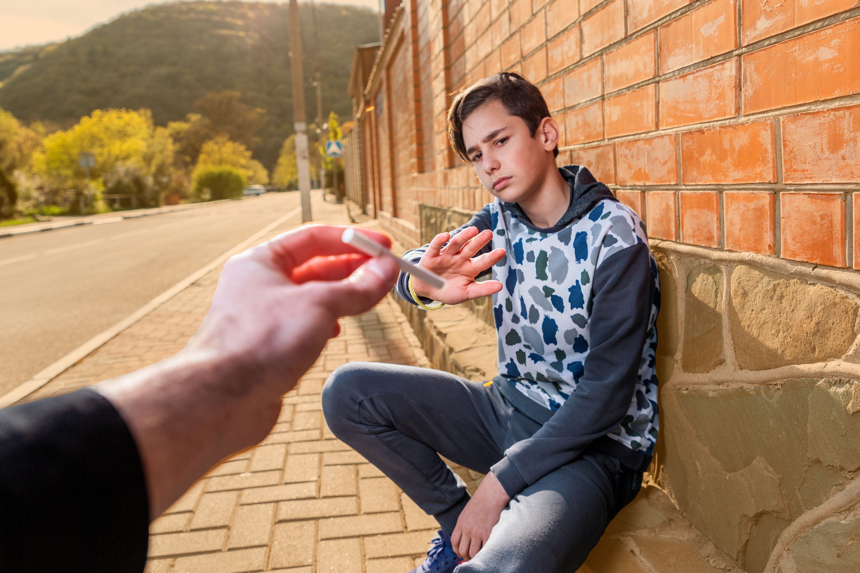 Jugendlicher, an einer Wand hockend, lehnt mit verneinender Geste eine Zigarette ab