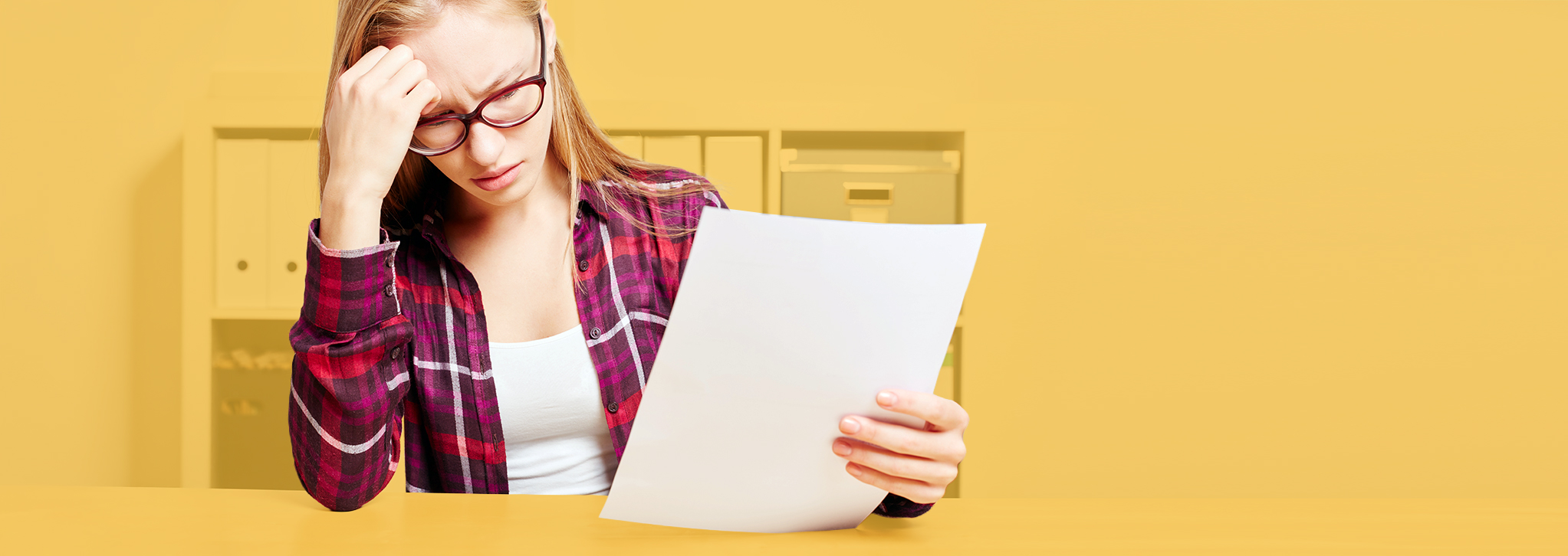 Junge Frau am Schreibtisch sitzend liest etwas auf einem Blatt Papier