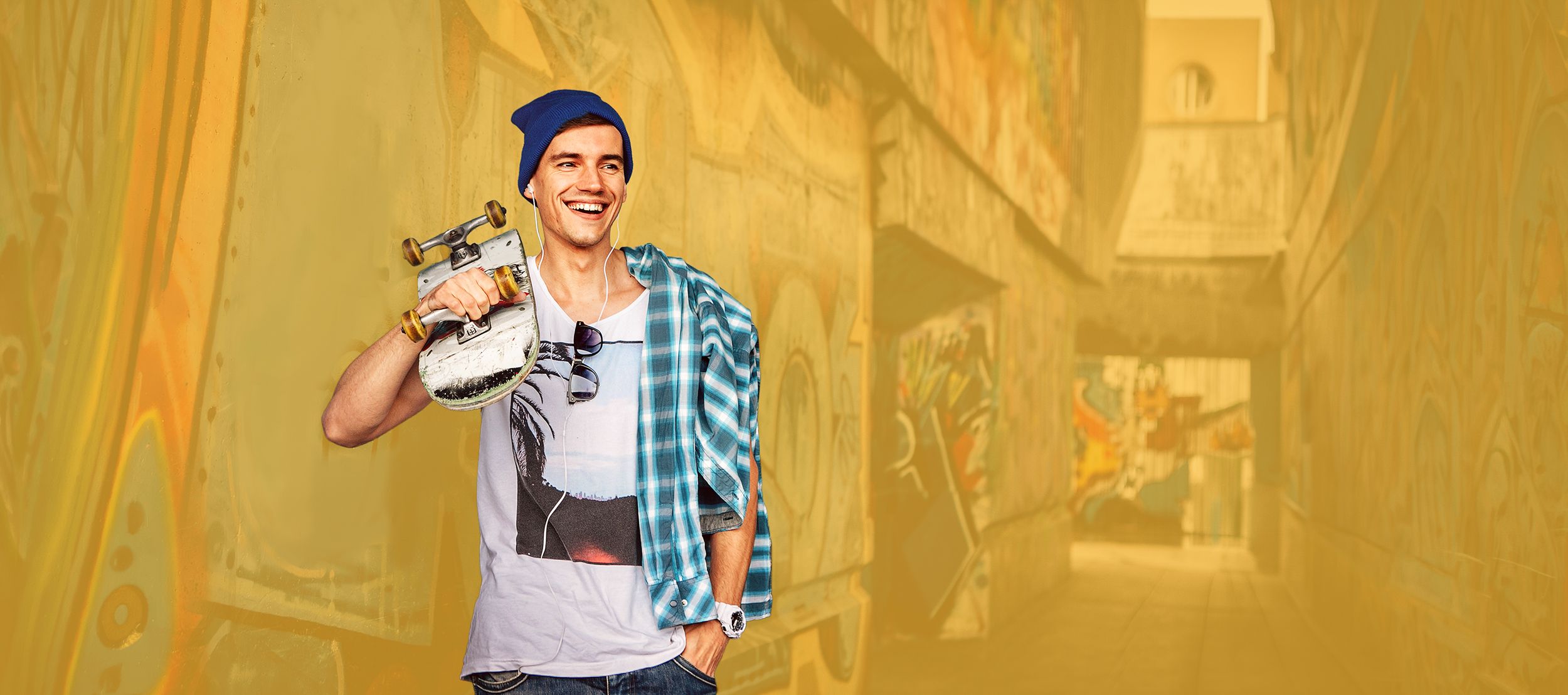 Junger Skater steht mit Skateboard an einer Hauswand	