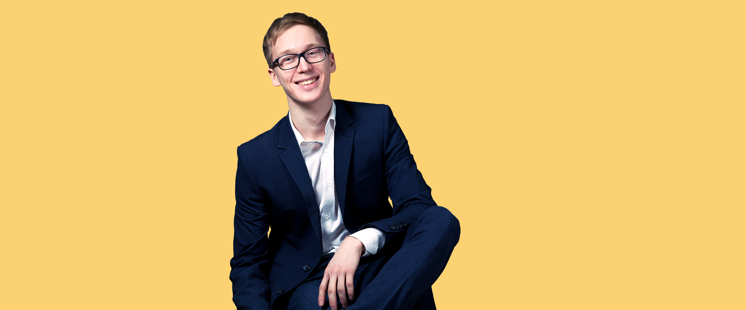 Sitzender Jugendlicher im Anzug mit Brille und gepflegtem Haar