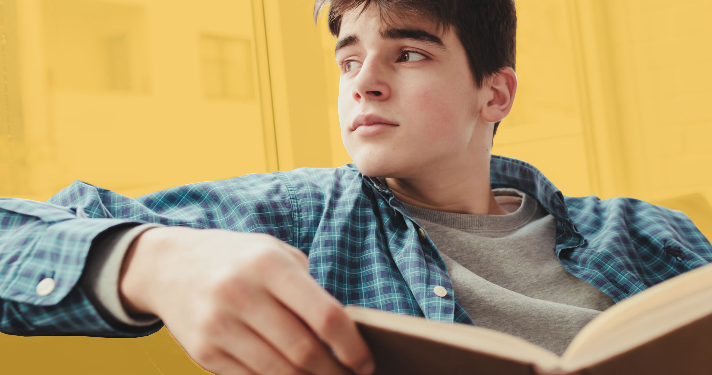 Jugendlicher sitzt verträumt auf einem Sofa und hält ein Buch