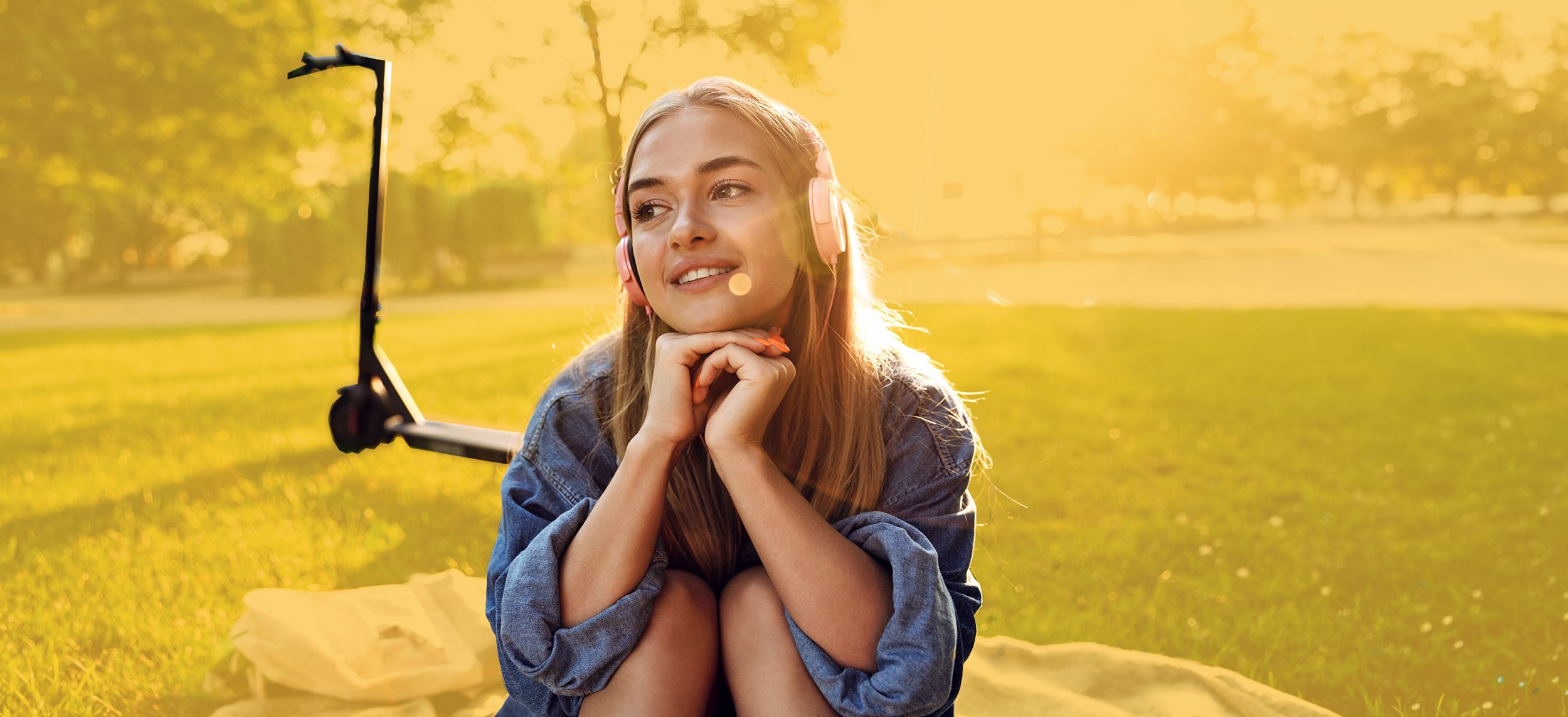 Jugendliche mit Kopfhörern und eRoller sitzt auf einer Decke im Park