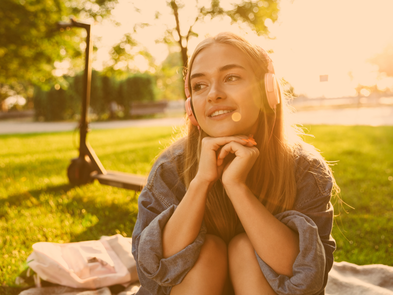 Jugendliche lieg mit Kopfhörern liegt im Park auf der Wiese und im Hintergrund steht ein eRoller