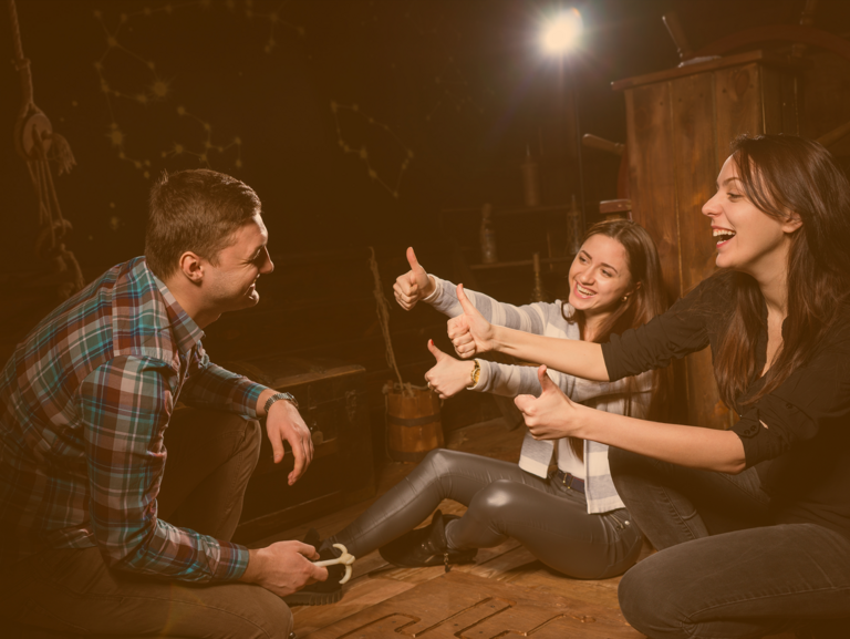 Zwei Mädchen und ein Junge sitzen am Boden eines dunklen Raumes und Lachen zusammen