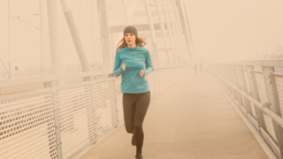 Junge Frau joggt im kühlen Nebel über eine Brücke