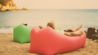 Zwei Jugendliche liegen am Strand auf bunten Luft-Sofas und schauen aufs Meer