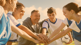 Jugendliche eines Sportteams und ihr Trainer legen alle in der Mitte fröhlich die Hände übereinander