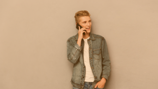 Jugendlicher lehnt an einer Wand, telefonierend lächelt er zufrieden
