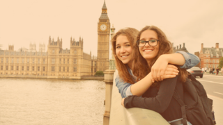 Zwei Teenagerinnen stehen freundschaftlich verbunden auf der Brücke vor Big Ben in London