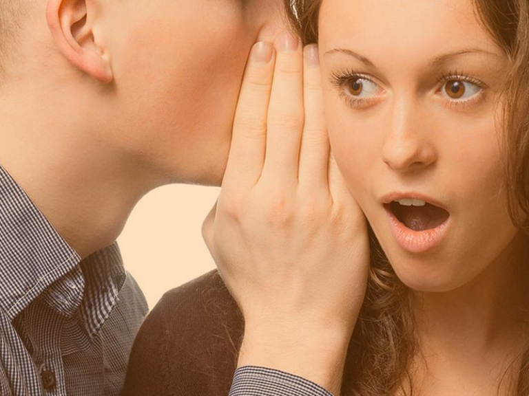 Jugendlicher tuschelt einer jungen Frau etwas ins Ohr