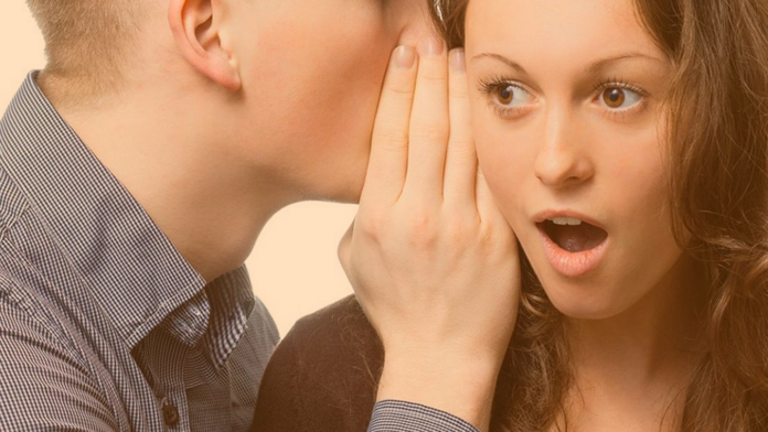 Jugendlicher tuschelt einer jungen Frau etwas ins Ohr