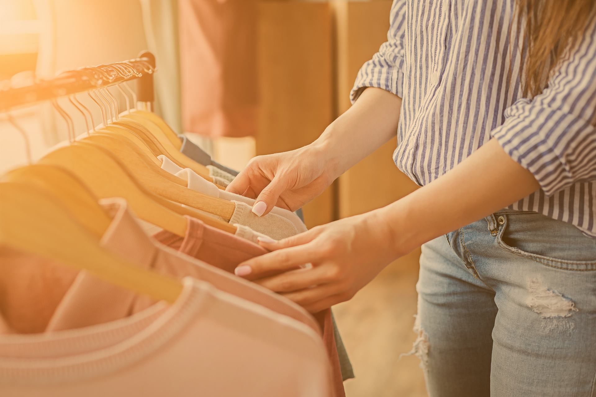 Junge Frau in Jeans sieht Kleiderständer mit nachhaltigen Produkten im Ladengeschäft durch