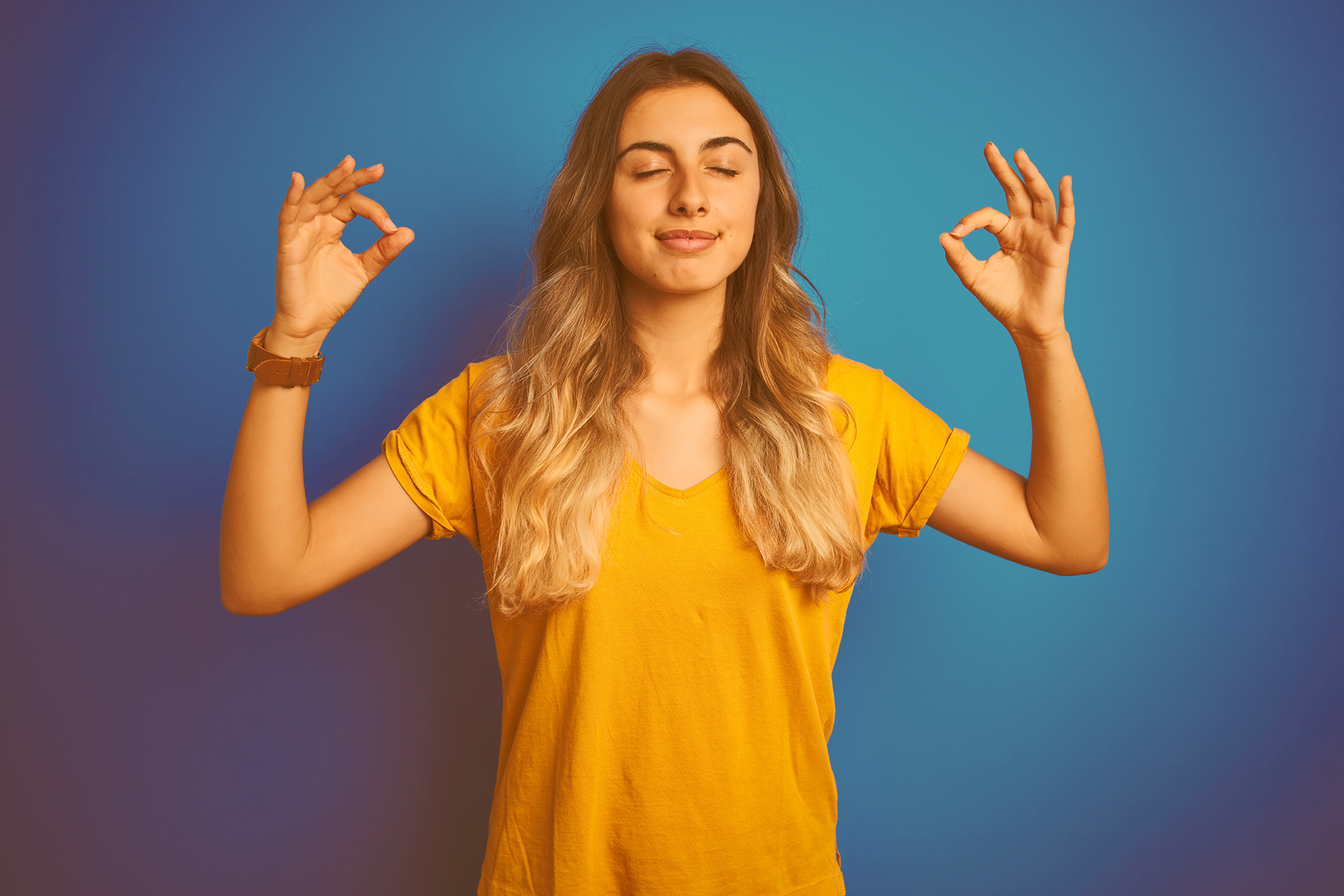 Junges Mädchen mit langen Haaren steh mit geschlossenen Augen und gehobenen Armen, während sie beidseitig das Gyan Mudra mit ihren Händen macht