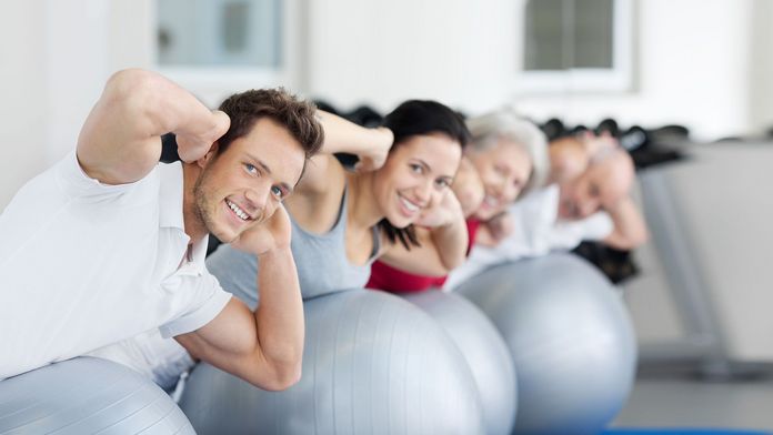 Sportliche Neujahrsvorsätze Männer und Frauen liegen bäuchlings auf Gymnastikbällen und haben die Händen hinter dem Kopf verschränkt
