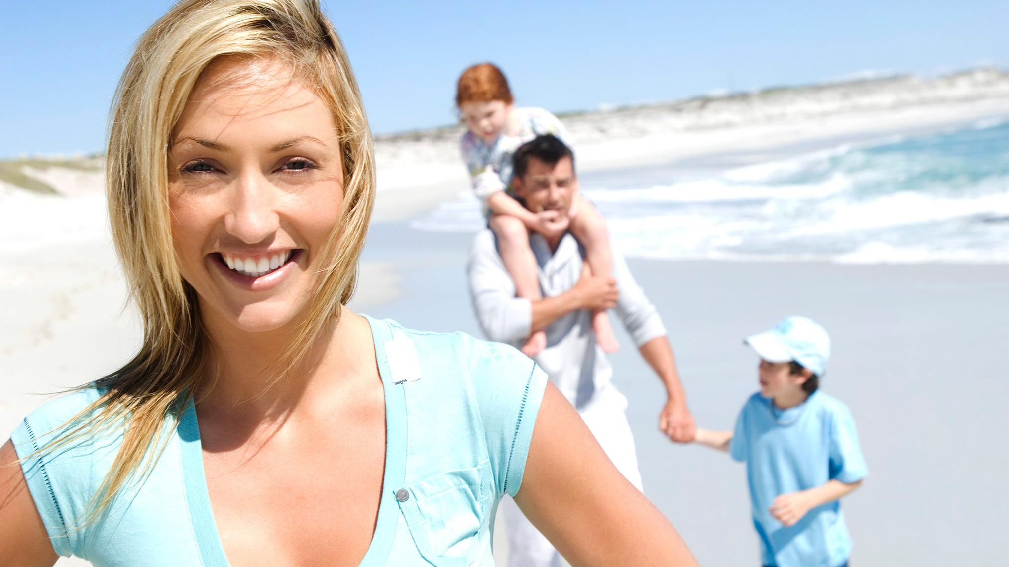 Die IKK als Familienversicherung Frau lächelt in die Kamera mit Familie am Strand