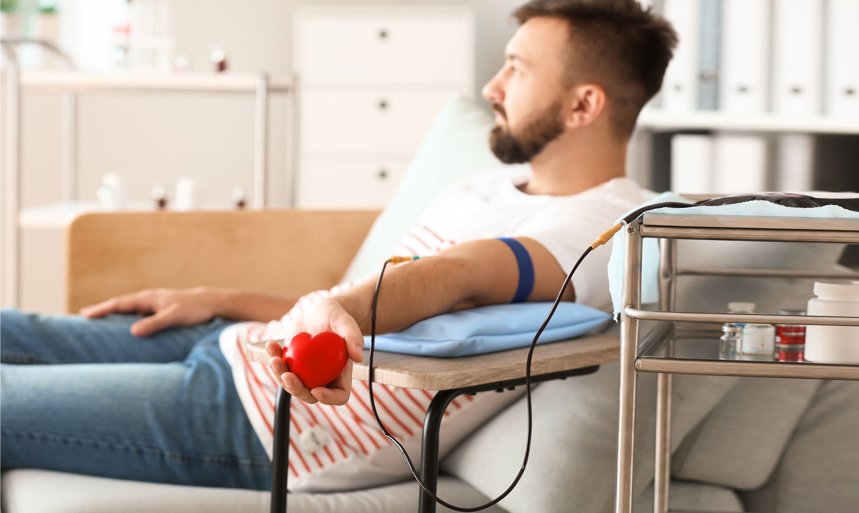 Blutspende – Leben retten Mann sitzt bei der Blutspende und hält ein rotes kleines Herz in der Hand